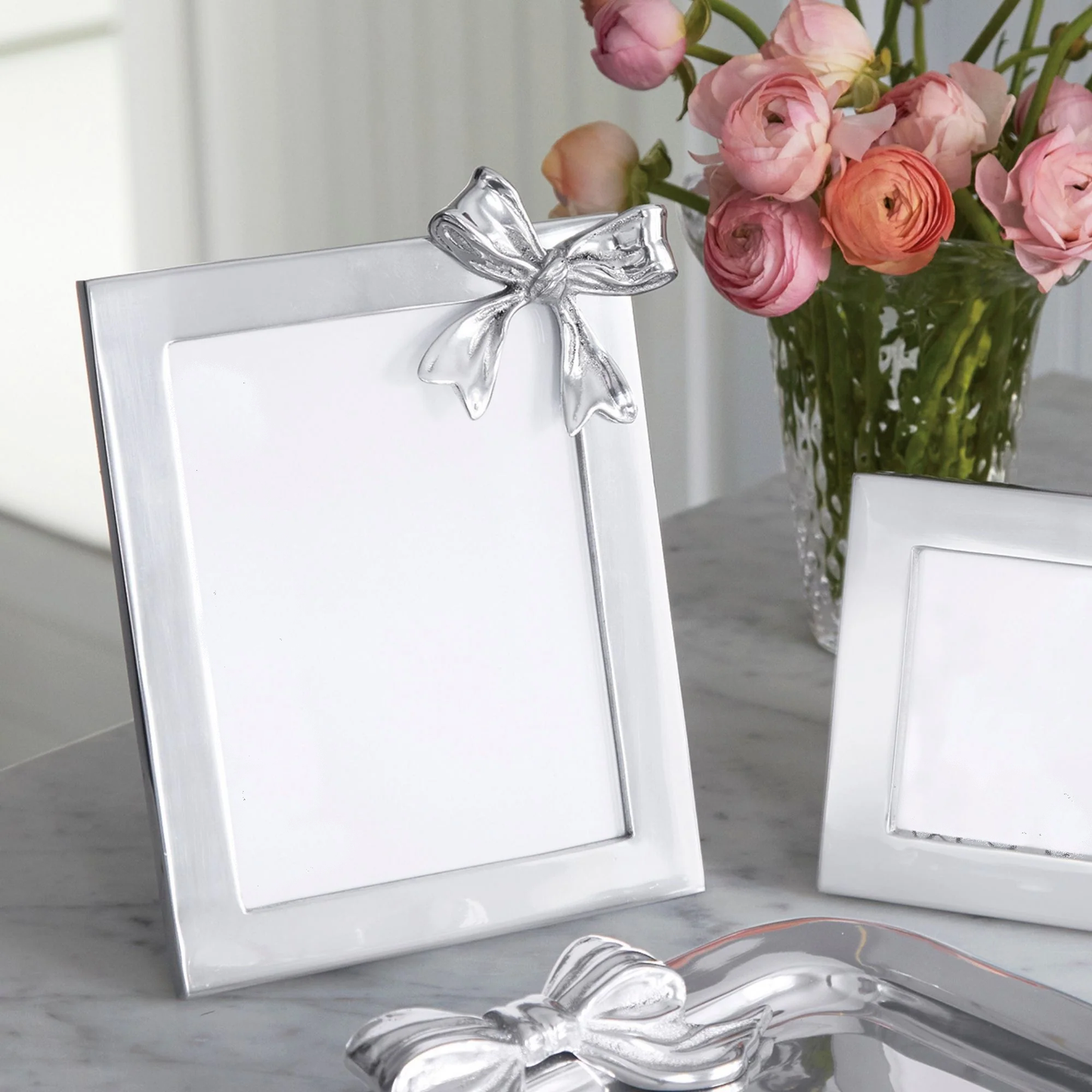 Silver photo frame with a bow on a marble surface with flowers in the background
