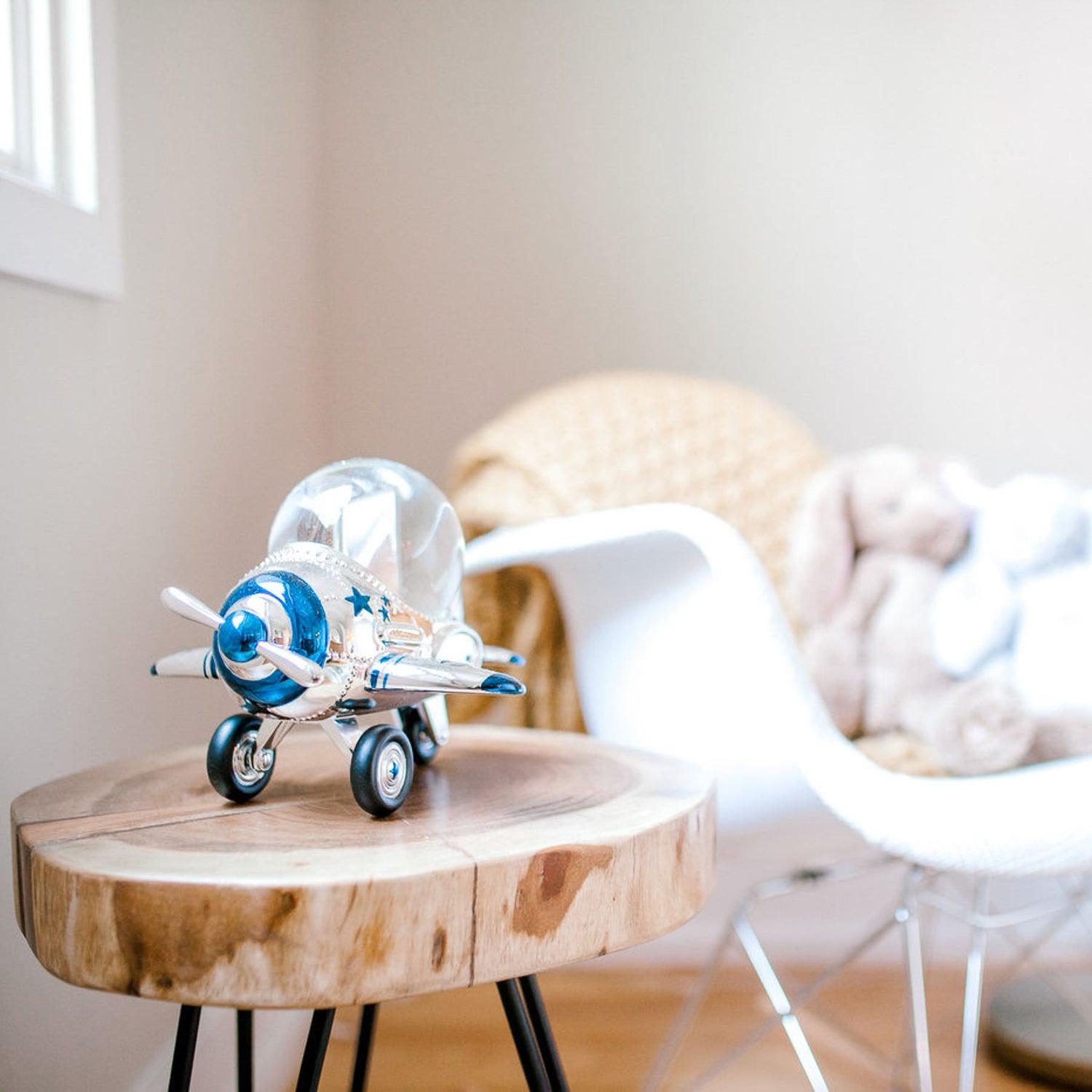 toy airplane on a stool sitting beside a white chair with a stuffed bunny on it