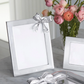 Silver photo frame with a bow on a marble surface with flowers in the background