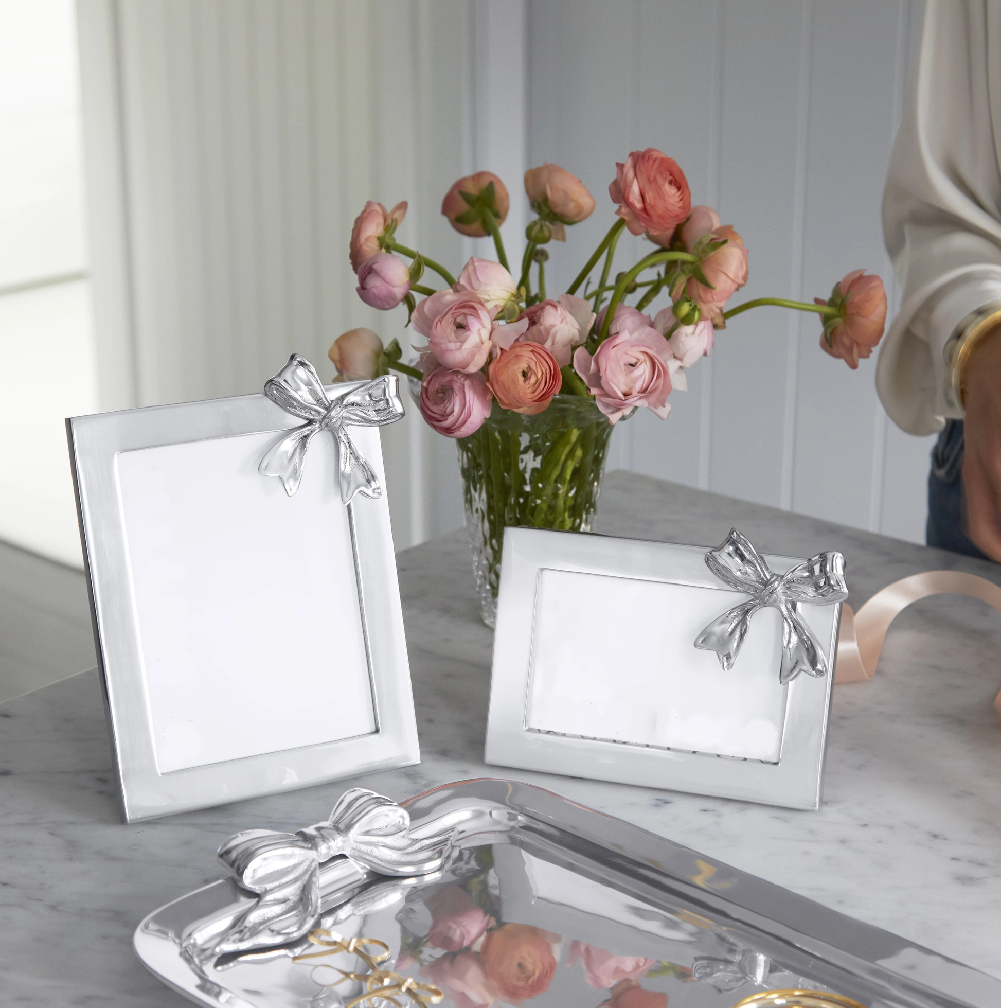Silver photo frames with bow accents on a table with pink flowers in the background